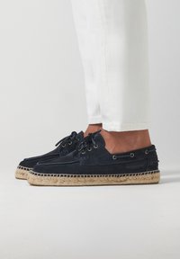 Chaussures en suède bleu marine à lacets avec semelle en jute tressé, dotées d'œillets en métal et d'une texture lisse. Convient pour une tenue décontractée.