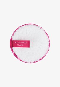 Disco desmaquillante circular con una superficie blanca, suave y esponjosa, y un borde de tela rosa brillante. Cuenta con una etiqueta rosa que dice "brush works REMOVE."