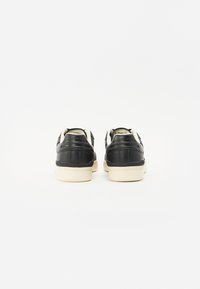 Black leather sneakers with a cream rubber sole, featuring a smooth texture, rounded shape, and minimalistic design.