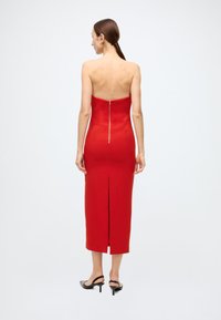 Red strapless midi dress with a fitted bodice, back zipper, and a slit at the hem. Smooth fabric with a slight sheen.