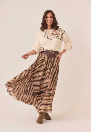 Suéter beige con textura floral, combinado con una maxi falda a rayas fluida en tonos tierra. Botas de ante marrón hasta el tobillo completan el conjunto.