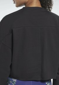 Felpa nera corta con un design semplice, caratterizzata da una cucitura visibile che attraversa la parte superiore della schiena e una texture morbida.