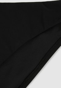 Fekete szövet közelről, az él mentén látható varrásokkal, mely a sima felületen a textúrát és az illesztés részleteit mutatja.