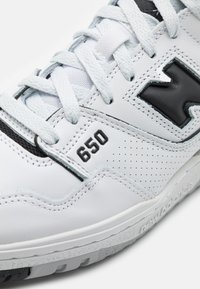 Sneaker bianca con accenti neri, dotata di una tomaia in pelle liscia, sezioni perforate e lacci. Mostra il numero "650" di lato.