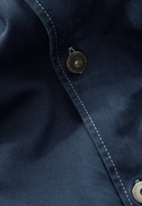 Gros plan sur un tissu bleu foncé avec des coutures blanches et un bouton-pression en métal visible sur la surface textile.