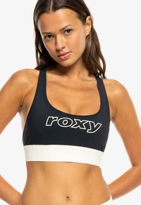 Čierny športový podprsenka so širokým elastickým pásom biely. Obsahuje veľké logo "roxy" v bielej farbe. Hladká tkanina, stredne široké ramienka a priliehavý strih.