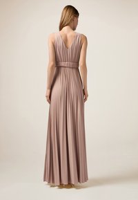 Langes, plissiertes Kleid in einem sanften, gedeckten Rosa mit einem V-Ausschnitt und gerafftem Taillenbund, aus strukturiertem Stoff, der elegant fällt.