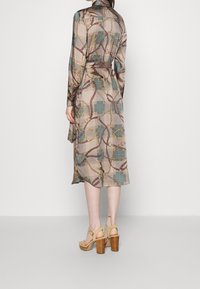 Långärmad klänning i en beige rutmönster med guldkedjeaccenter. Tyget har en slät yta och en design med bälte i midjan.