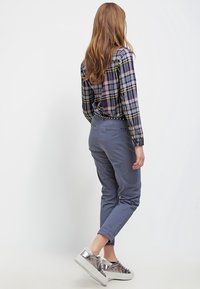 Kostkovaná košile na knoflíky v námořnické modré, žluté a červené; šedé slim-fit kalhoty; metalické stříbrné tenisky. Hladká látka, ležérní design.