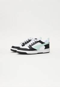 Pár bílých nízkých tenisek s černými akcenty a bledě zeleným pruhovaným designem na boku, bílé tkaničky a bílé podešve.