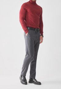 Pull à col roulé rouge, pantalon gris cintré avec ceinture, et chaussures en cuir noir. Accent sur un design élégant et ajusté ainsi qu'une combinaison de couleurs moderne.