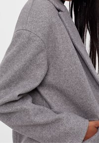 Šedé oversized sako z vlněné směsi s širokými klopami, měkkou texturou, spadnutými rameny a volným střihem, s bočními kapsami.