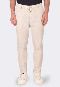 Pantaloni beige chiaro realizzati in un tessuto testurizzato, con vita regolabile tramite cordoncino, tasche laterali e un design slim fit. Indossati con sneakers bianche.