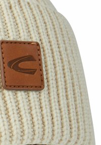 Creme strikket hue med vertikal ribbende mønster, prydet med et brunt lædermærke med et præget logo, der forbedrer teksturen og designet.