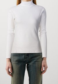 Weißes, geripptes Rollkragenoberteil mit langen Ärmeln und enganliegendem Design. Kombiniert mit Jeans aus Denim in verblassten Farbtönen und geradem Schnitt.