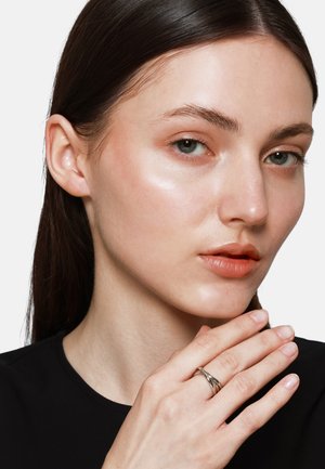 Zilveren gedraaide ring om de wijsvinger; model heeft gladde huid met lichte makeup, draagt een zwarte shirt, heeft lang donker haar en een neutrale lipkleur.