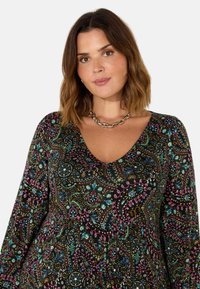 Černé šaty s dlouhým rukávem, zdobené pestrým paisley vzorem v modré, růžové a zlaté barvě. V-výstřih a uvolněný střih. Stříbrný řetízek na krk.