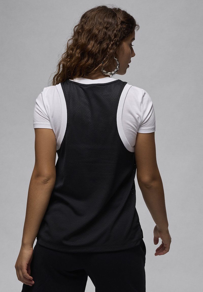 Schwarzes, mesh-förmiges Sporttanktop mit hohem Kragen und weiten Armausschnitten, über einem weißen T-Shirt getragen. Strukturierter Stoff, atmungsaktives Design.