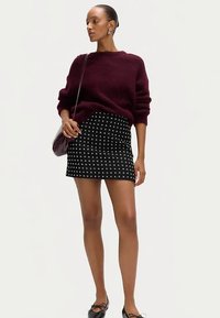 Bordowy, gruby sweter na drutach zestawiony z czarną mini spódnicą z białym wzorem krzyża. Całość uzupełniona czarnymi balerinami i torebką na ramię.