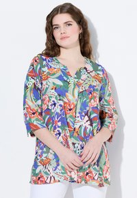 Tunic floreale con una base verde e diverse fantasie colorate. Presenta un colletto a V, maniche a tre quarti e una vestibilità ampia. Tessuto a trama.