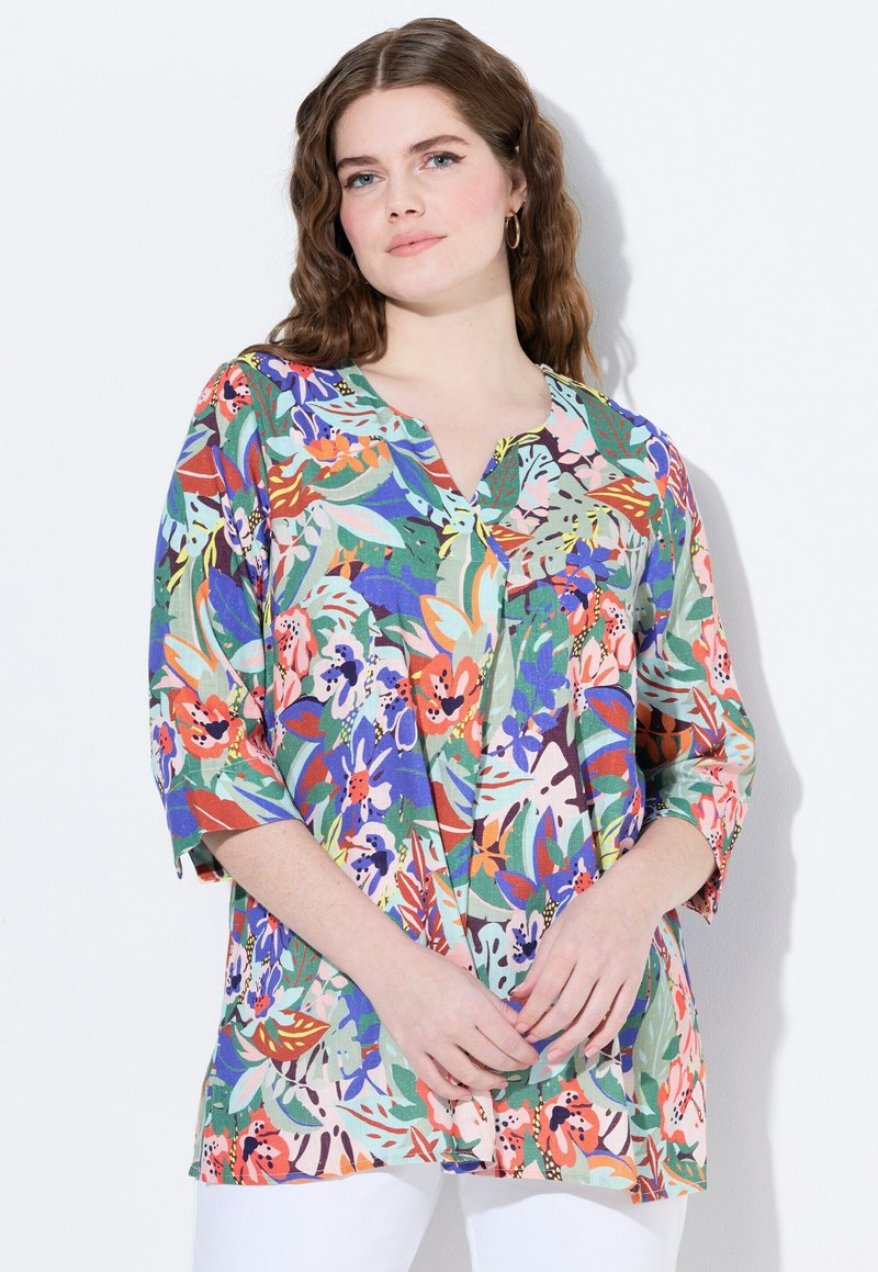 Tunic floreale con una base verde e diverse fantasie colorate. Presenta un colletto a V, maniche a tre quarti e una vestibilità ampia. Tessuto a trama.