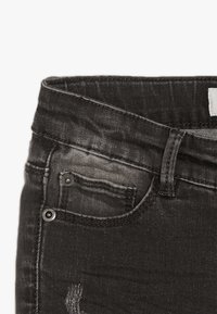 Jeans de mezclilla negra con una textura desgastada, que presentan un cierre de botón y cremallera, bolsillo frontal y costuras en contraste.