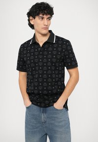 Camiseta tipo polo negra con patrón de logotipos repetidos, manga corta y cuello blanco contrastante. Material de algodón suave, ajuste relajado.