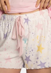 Shorts blancs avec des motifs d'étoiles roses, violettes et jaunes, dotés d'une taille élastique avec cordon de serrage et d'un tissu doux et texturé.