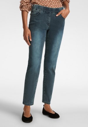 Dunkelblaue Denim-Jeans mit Slim-Fit, elastischem Bund, Vordertaschen und glatter Textur, kombiniert mit schwarzen flachen Schuhen.