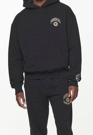 Hoodie noir en coton, avec une poche kangourou à l'avant, des poignets côtelés et des accents de logo brodés en or. Associé à un pantalon noir assorti.