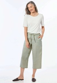 Witte blouse met korte mouwen, gecombineerd met lichtgroene, enkellange, met trekkoord verstelbare broek. Gestructureerde stof en een eenvoudig, ontspannen ontwerp. Zwarte instap schoenen.