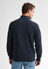 Donkerblauwe gebreide trui met hoge kraag, lange mouwen en een aansluitende fit, gecombineerd met lichtblauwe denim jeans.