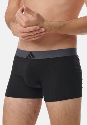 Boxer-briefs noirs en tissu doux, avec une ceinture élastique grise à surface texturée et un discret logo sur le devant.