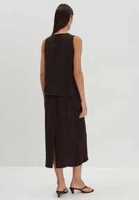 Top senza maniche marrone abbinato a una gonna midi coordinata con uno spacco laterale, realizzata in un tessuto morbido con un design semplice ed elegante.