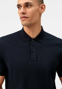 Dunkelblaues Poloshirt aus strukturiertem Stoff, mit kurzen Ärmeln und einem Kragen. Verfügt über eine Knopfleiste mit zwei schwarzen Knöpfen.