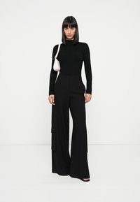 Black, fitted long-sleeve top paired with wide-leg black trousers featuring side cargo pockets, complemented by a small light pink handbag.