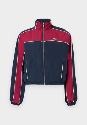 Afgesneden jas in marineblauwe en rode stof met witte accenten, hoge kraag, ritssluiting en zijzakken. Glad textuur, sportief design.