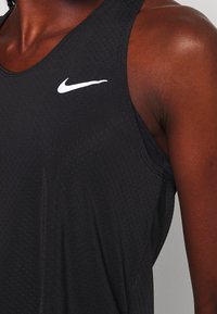 Canottiera sportiva nera in tessuto testurizzato, con il logo swoosh bianco di Nike nella parte superiore sinistra del petto e un design minimalista.