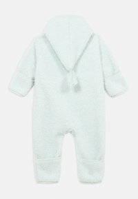 Combinaison en polaire bleu clair et douce avec capuche, présentant un détail à pompons et des poignets élastiques. Texture lisse, conçue pour le confort et la chaleur.