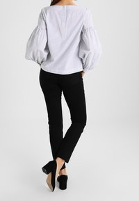 Blouse rayée blanche et bleue avec manches bouffantes, fermeture par boutons à l'arrière, associée à un pantalon noir et des talons. Tissu lisse et coupe décontractée.