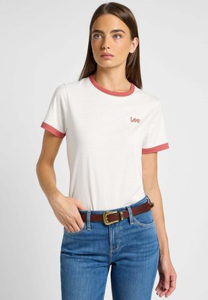 T-shirt bianca in cotone con colletto e bordi delle maniche rossi, con un piccolo logo ricamato "Lee" sul petto, abbinata a jeans blu.