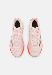 Scarpe da ginnastica rosa chiaro con tomaia in mesh, dettagli neri e suola arancione. Presentano lacci, colletto imbottito e logo vicino alla linguetta.