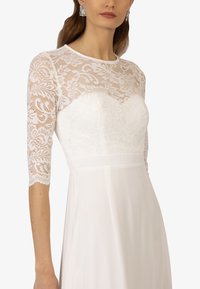 Witte jurk met een kant bodice met bloemenpatronen en driekwart mouwen. Glad stoffen rok met een aansluitende taille.