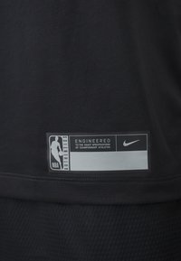 Étiquette NBA Authentics sur tissu noir avec logo Nike et texte « Conçu selon les spécifications exactes des athlètes champions. »