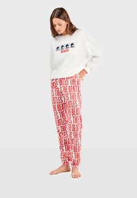 Sudadera blanca con estampado marino que presenta arte de los Beatles. Pantalones de pijama rojos con el texto repetido "THE BEATLES" en negrita de color blanco.