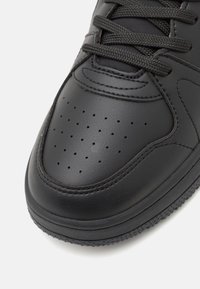 Sorte lædersneaker med perforeret tå, struktureret overflade, flade snørebånd og kontrasterende syninger, udstyret med en gummisål.