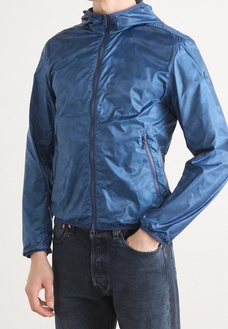 Navy blue zip-up jacket with a hood, made of shiny, lightweight material. Features side pockets and elastic cuffs. Smooth texture.