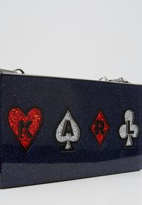 Navy glitter clutch featuring poker symbols in red and silver, with an embossed "KARL" design. Metallic chain strap included.