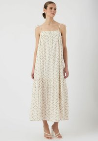 Blommig maxiklänning i krämfärg med tunna axelband och rosettdetaljer, med en rynkad byst och lager på lager-skirt. Mjuk, lättviktig tyg.