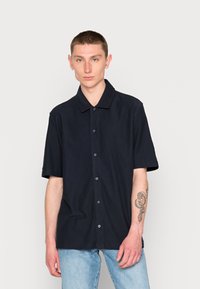 Camisa azul marinho de manga curta, com colarinho pontudo, feita de um tecido suave. Apresenta um corte descontraído e botões na parte da frente.